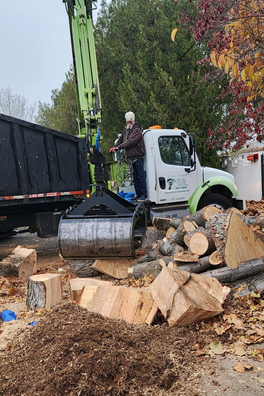Worker using grapple truck to pick-up large wood pieces from jobsite.